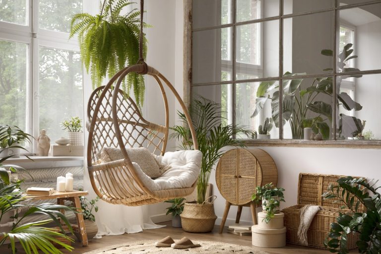 Fauteuil suspendu en rotin de style bohème dans une pièce fleurie. Décoration hippie DIY.